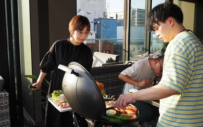 写真　社内イベント　バーベキューで、社員が肉を焼きながら談笑する様子